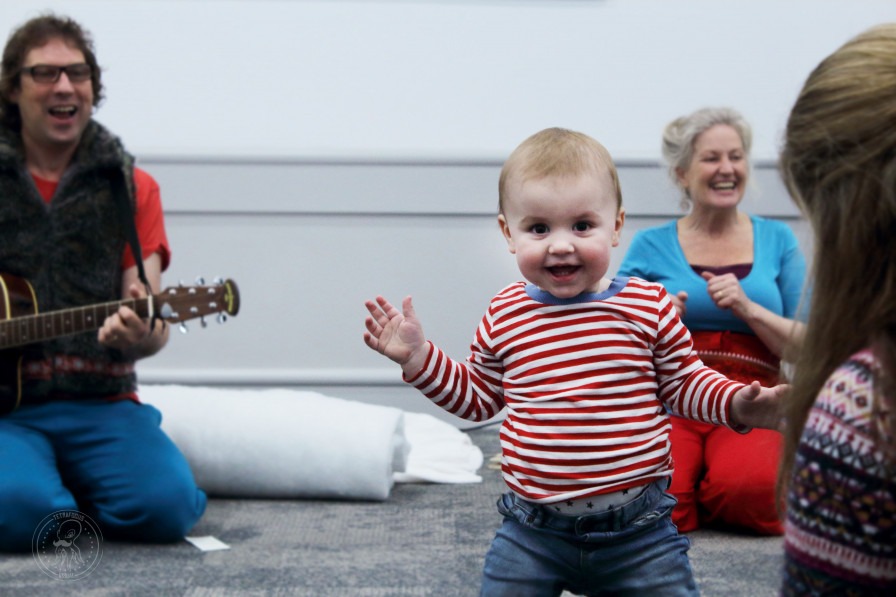 Cute baby running towards the camera, a person with a guitar out of view. 