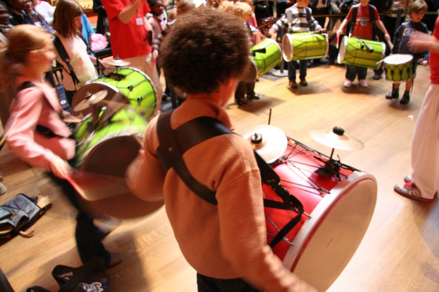A child holding a big drum which is strapped to them. 