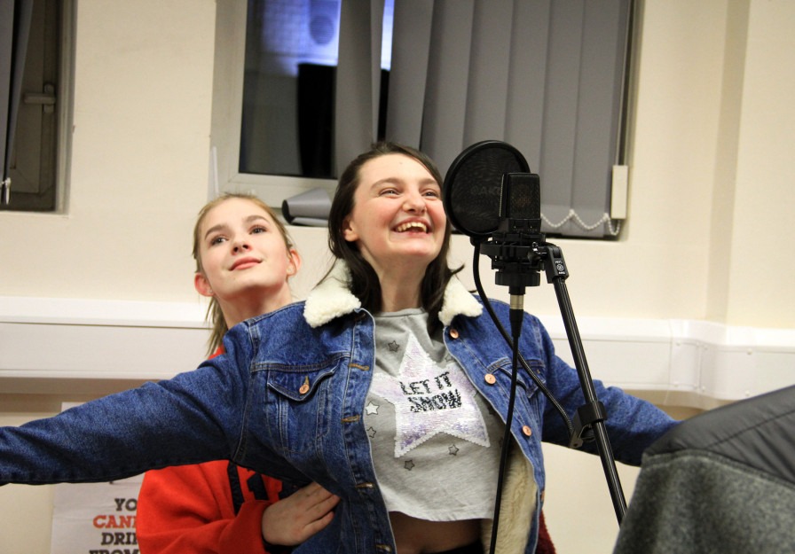 Photo shows one young person in front of a microphone and another behind them - Titanic-esque!