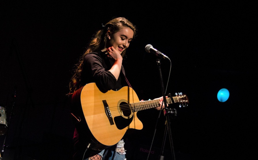 Image shows a young person with a guitar and a microphone