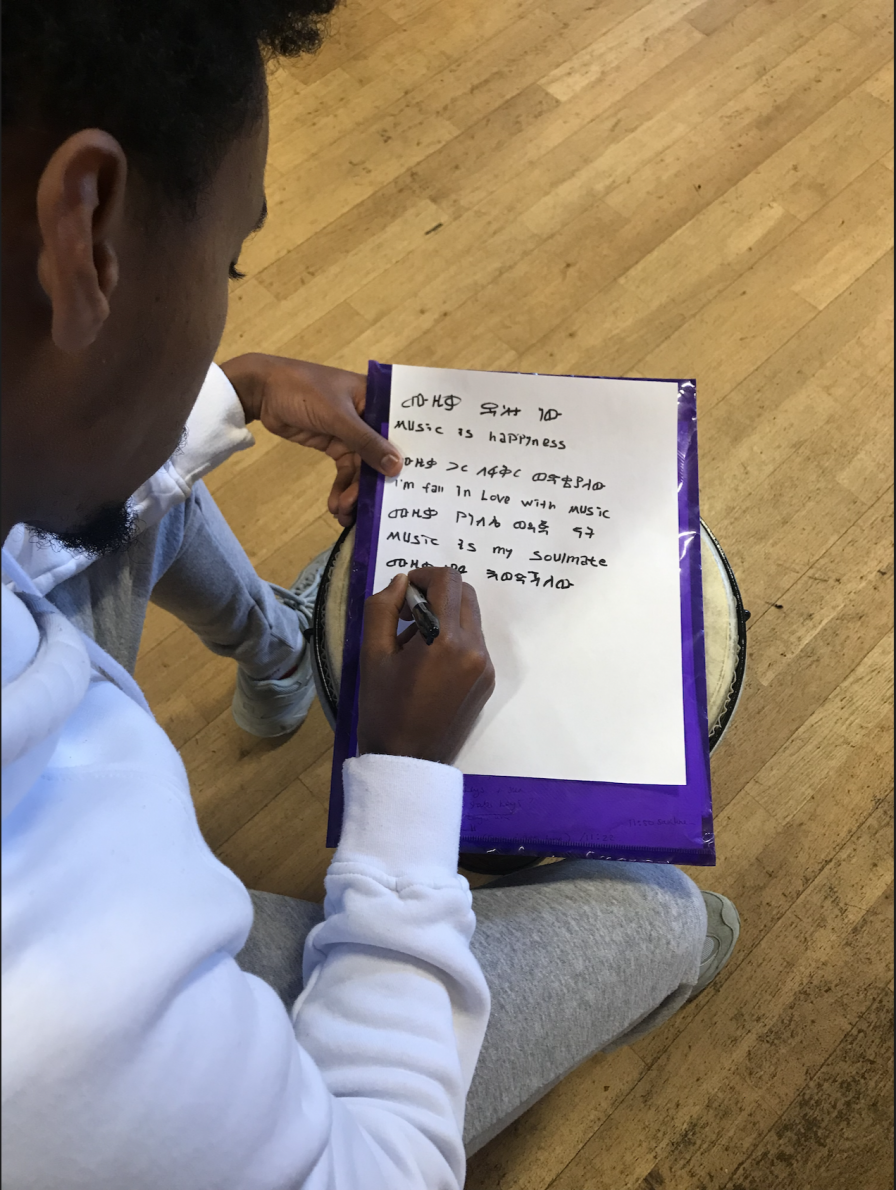A Music Connects participant begins to write his ideas for lyrics, starting with "Music is Happiness"