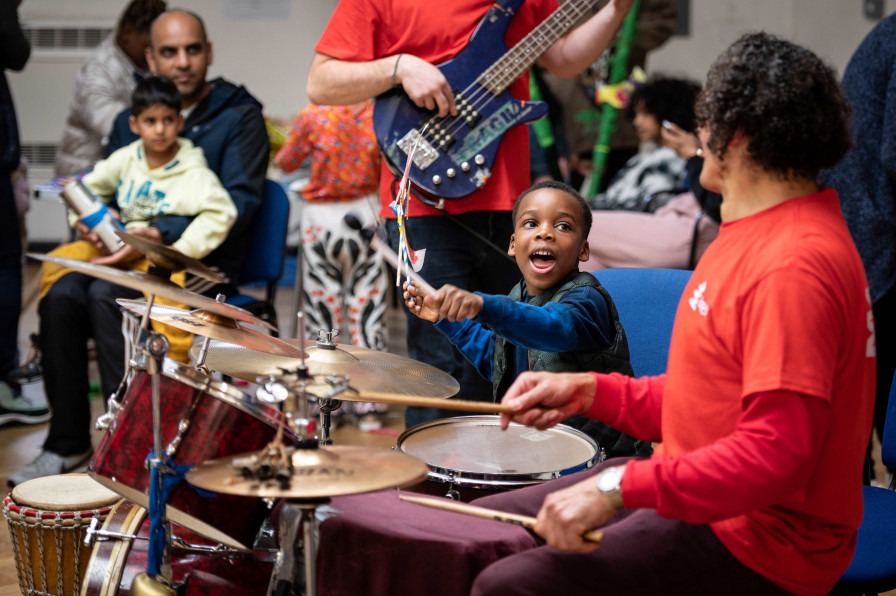 Young child playing the drums with a music leader