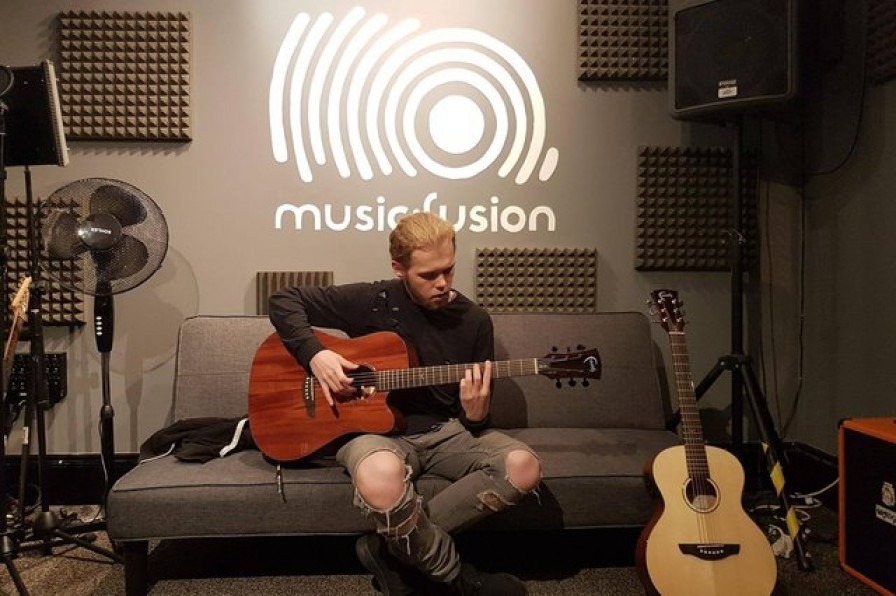 A young person sitting in a studio with an acoustic guitar