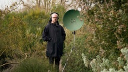 Gawain with a large parabolic microphone dish outside in nature. 