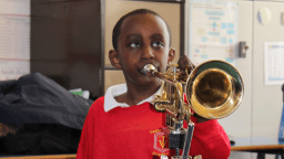 A boy plays a trumpet. He wears a red jumper. 