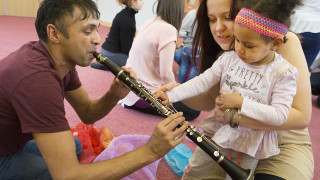 Music leader playing clarinet and young child reaching for it
